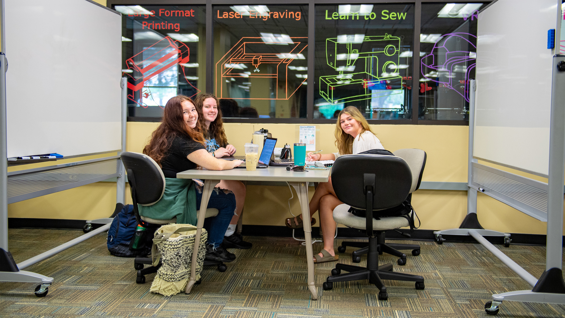 Three students studying at a desk, alongside whiteboards, at the MakerSpace.
