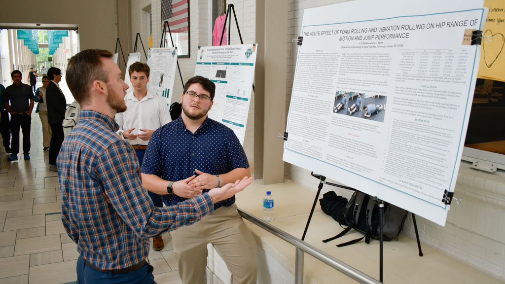A photo of a student presenting a research poster to a CCU exercise and sport science faculty